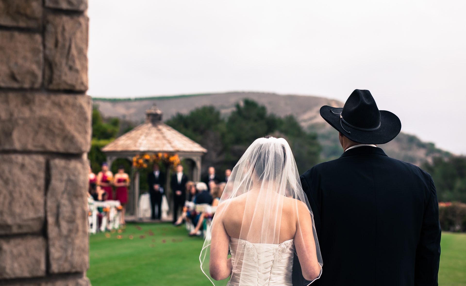 Woman in white walking arm in arm with a man in a black cowboy hat toward a garden gazebo at Glen Annie in Goleta