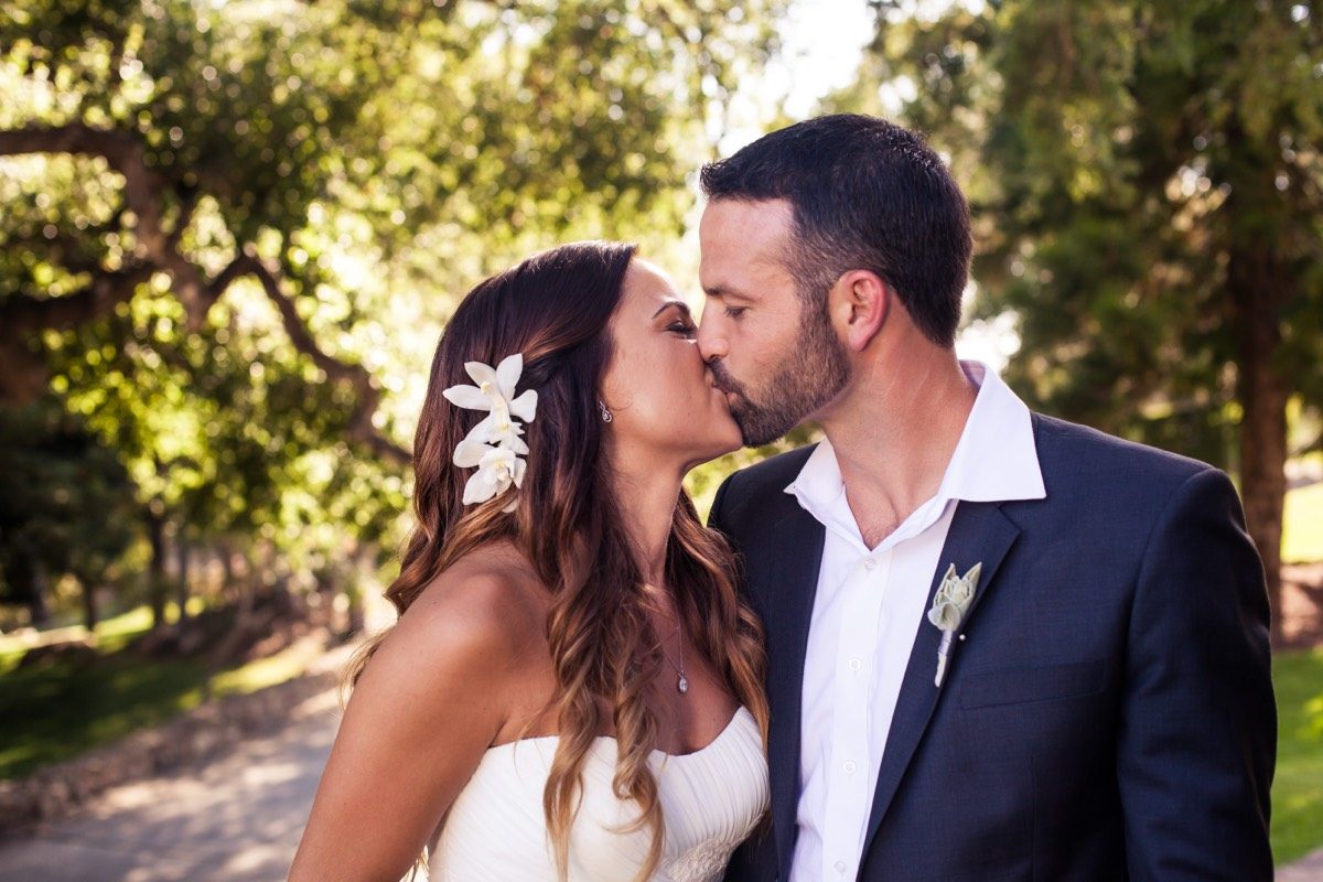 Couple kissing beneath oak trees, she in white with a flower in her hair