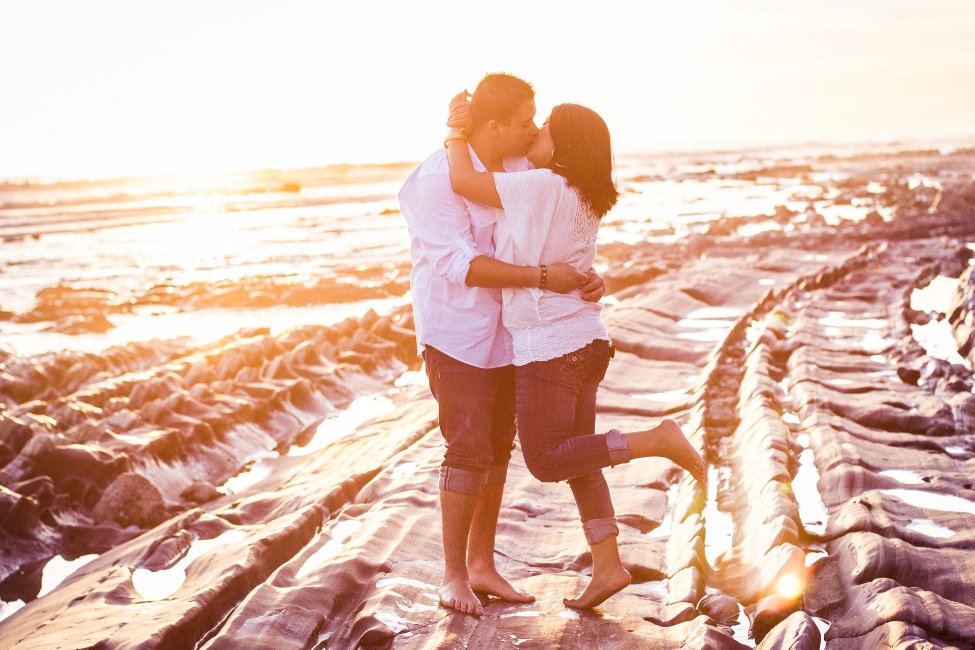 Engaged couple embracing on the tide-pool rocks at sunset