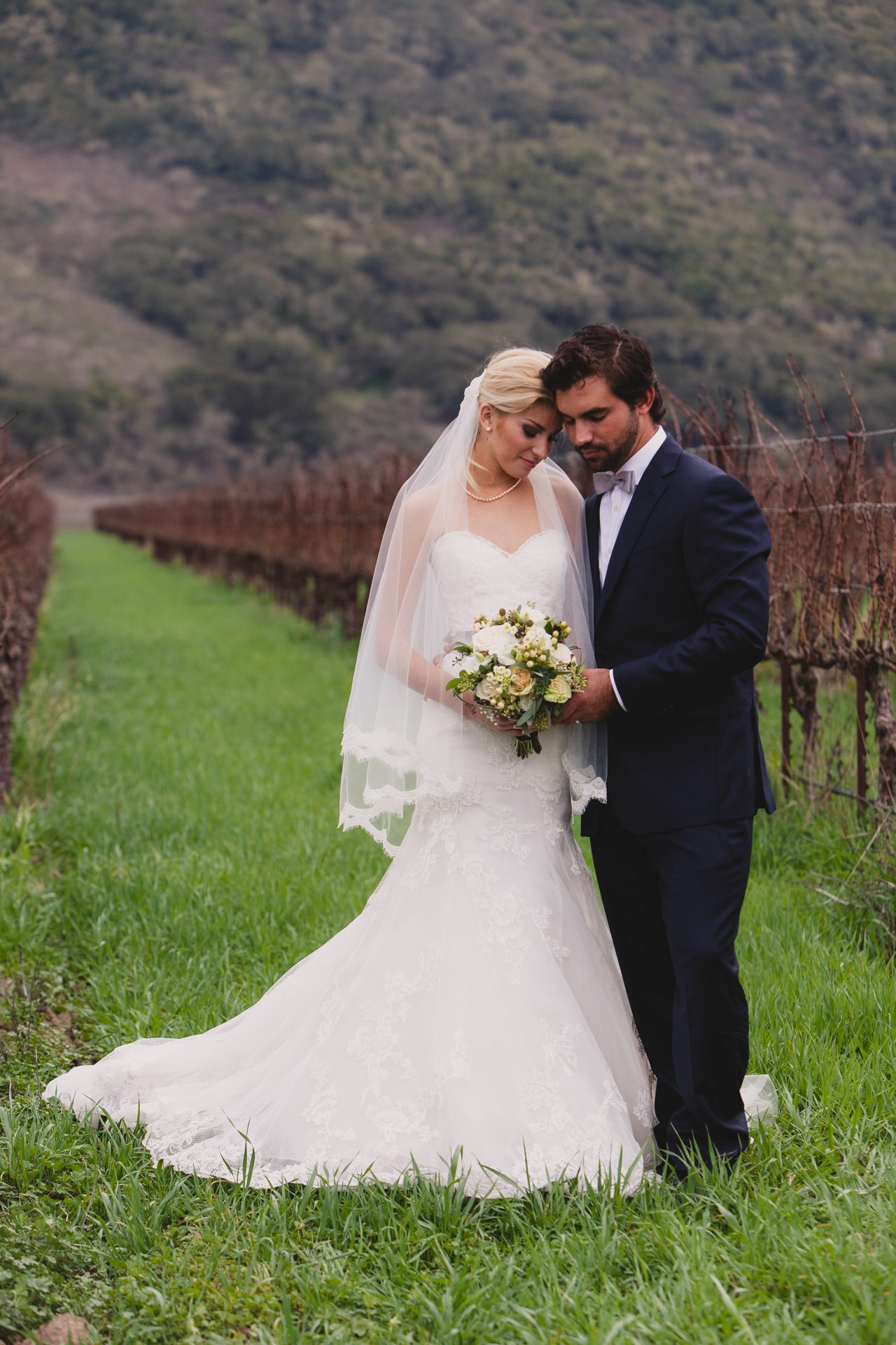 Couple standing together in a green vineyard row at Sanford Winery under soft overcast light