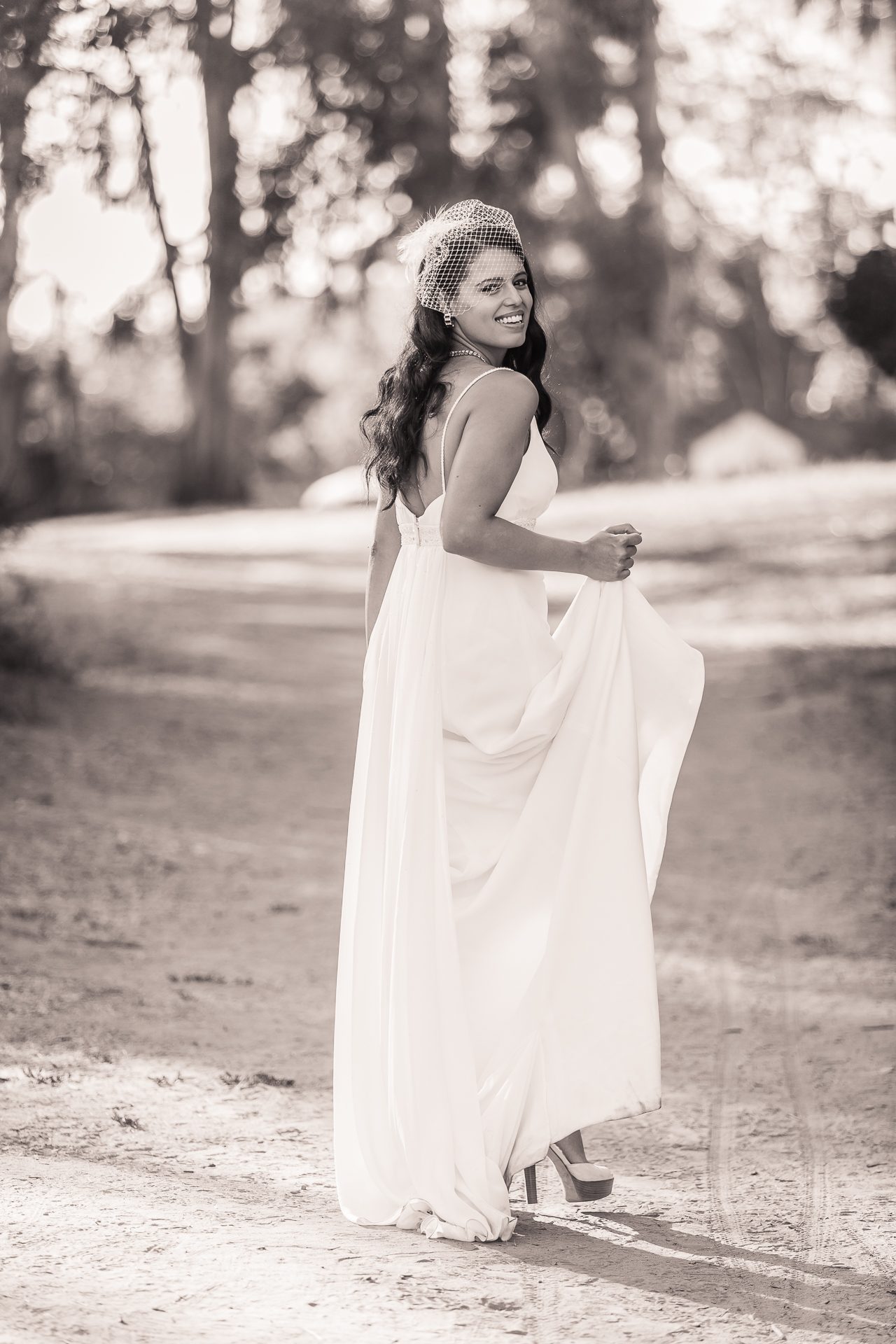 Sepia portrait of a woman in a long white dress walking a dirt path, smiling back over her shoulder