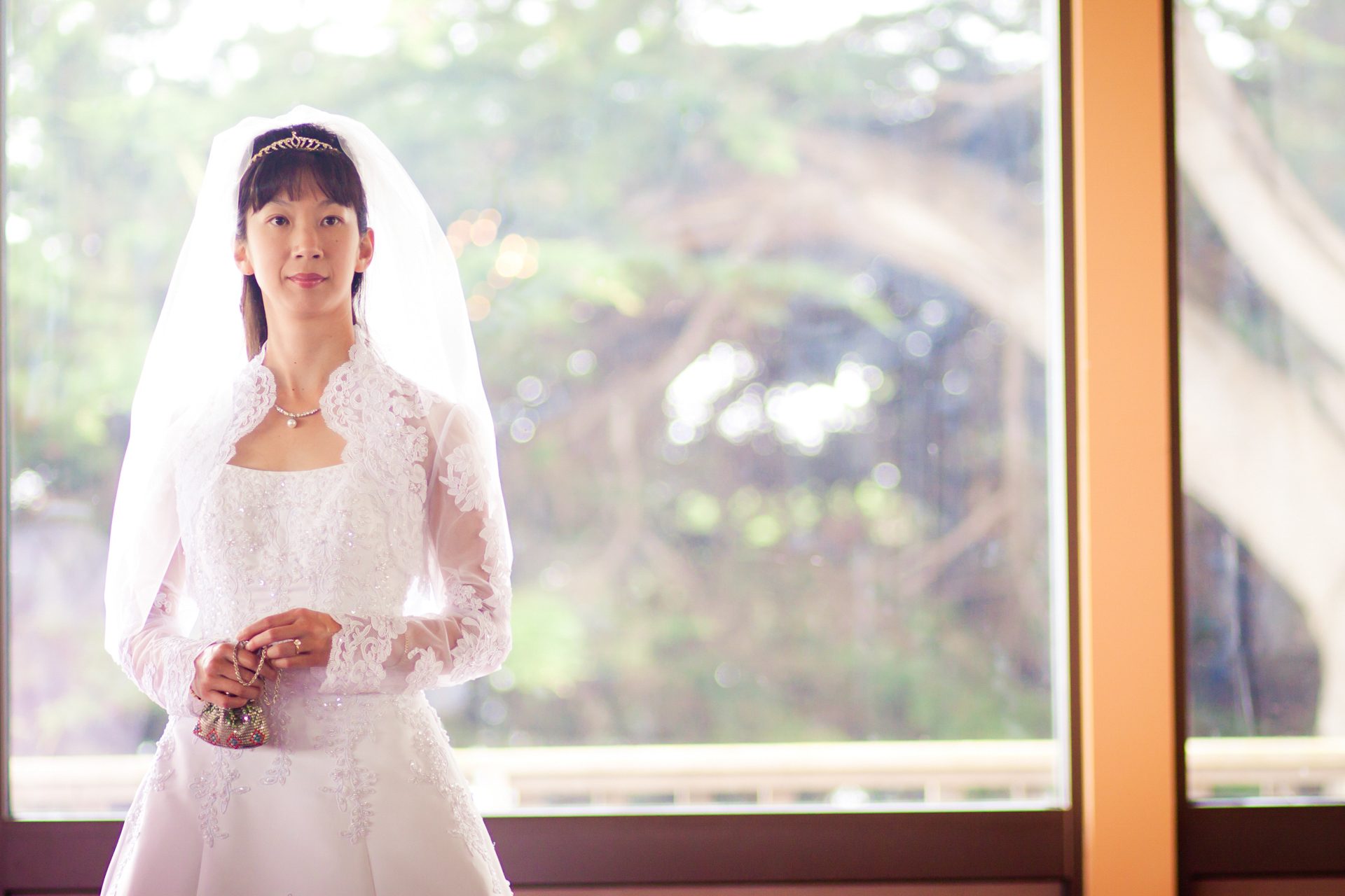 Woman in white lace standing by a bright window, holding flowers