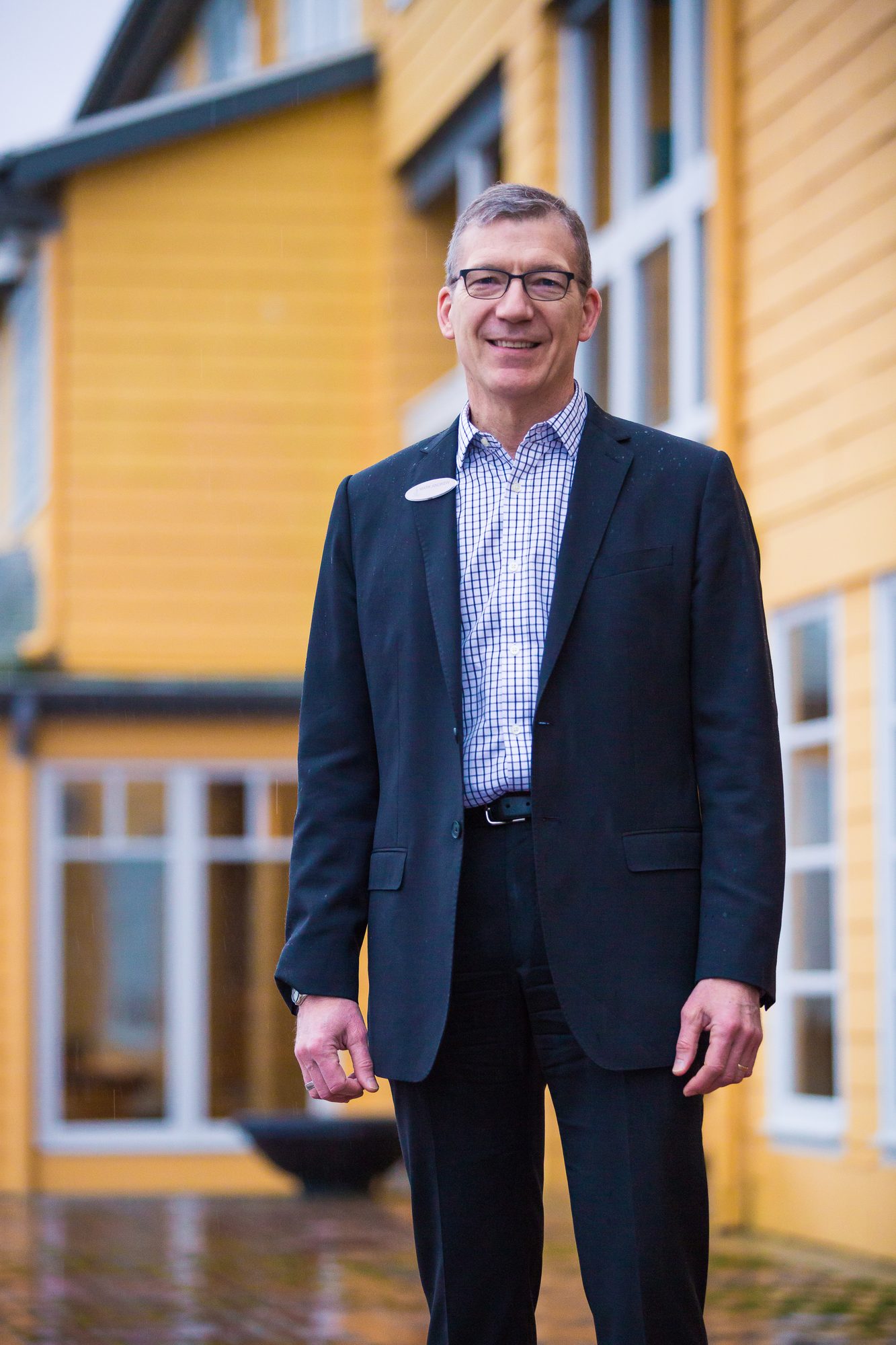 Businessman in a navy blazer standing in front of a yellow clapboard building