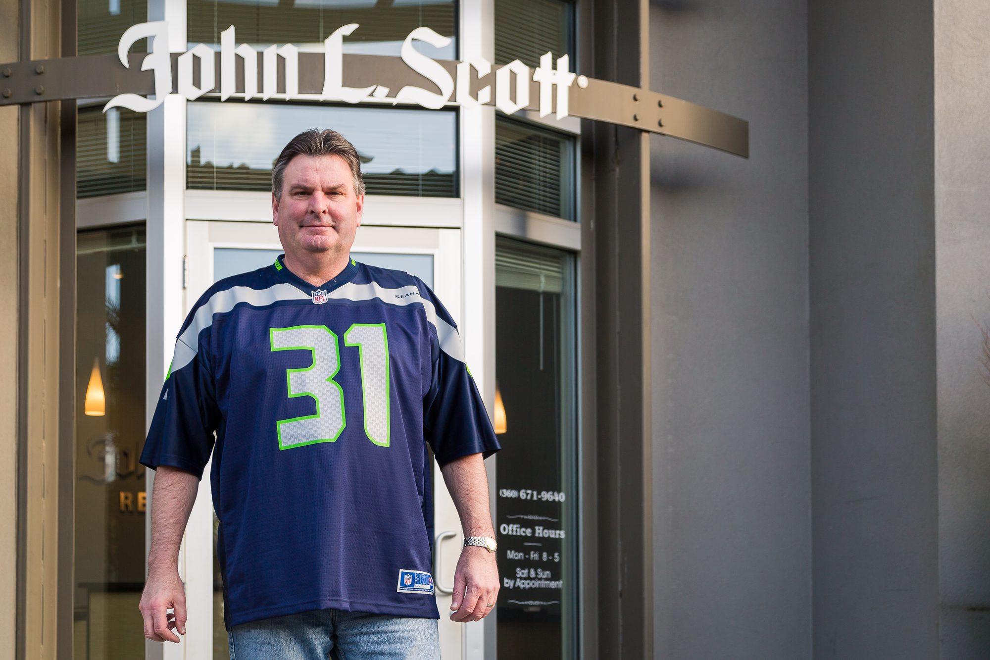 Real estate broker in a Seahawks jersey standing at his office entrance