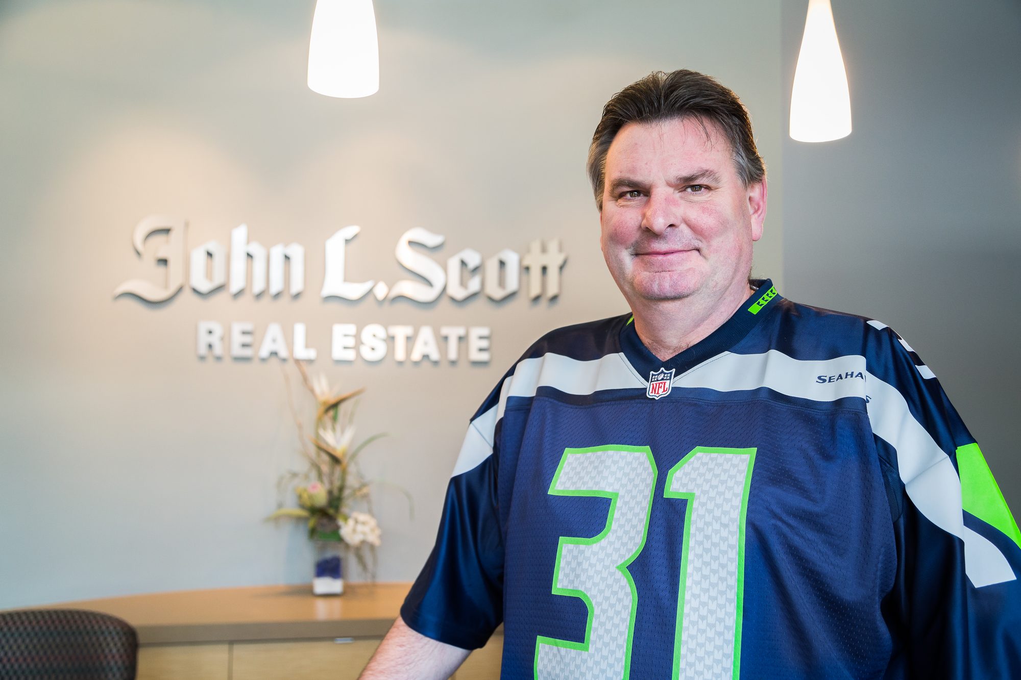 Smiling real estate broker in a Seahawks jersey in his office lobby