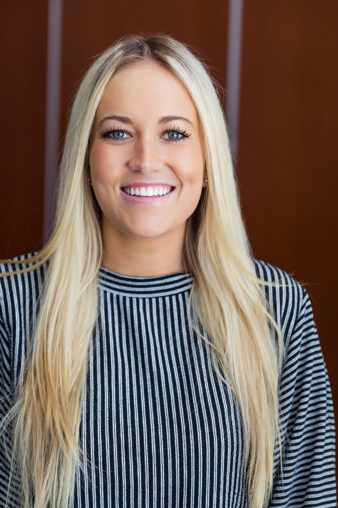 Smiling blonde woman in a striped top against a warm wood wall