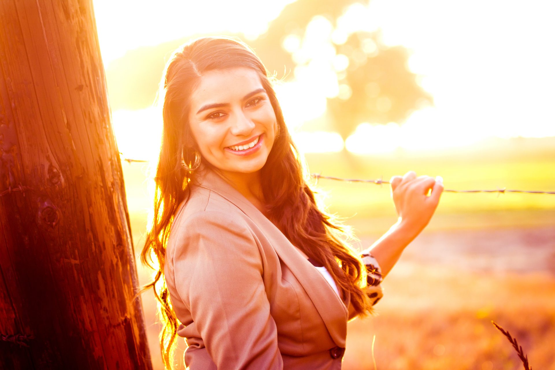 Young woman smiling beside a fence post as the sun sets behind her