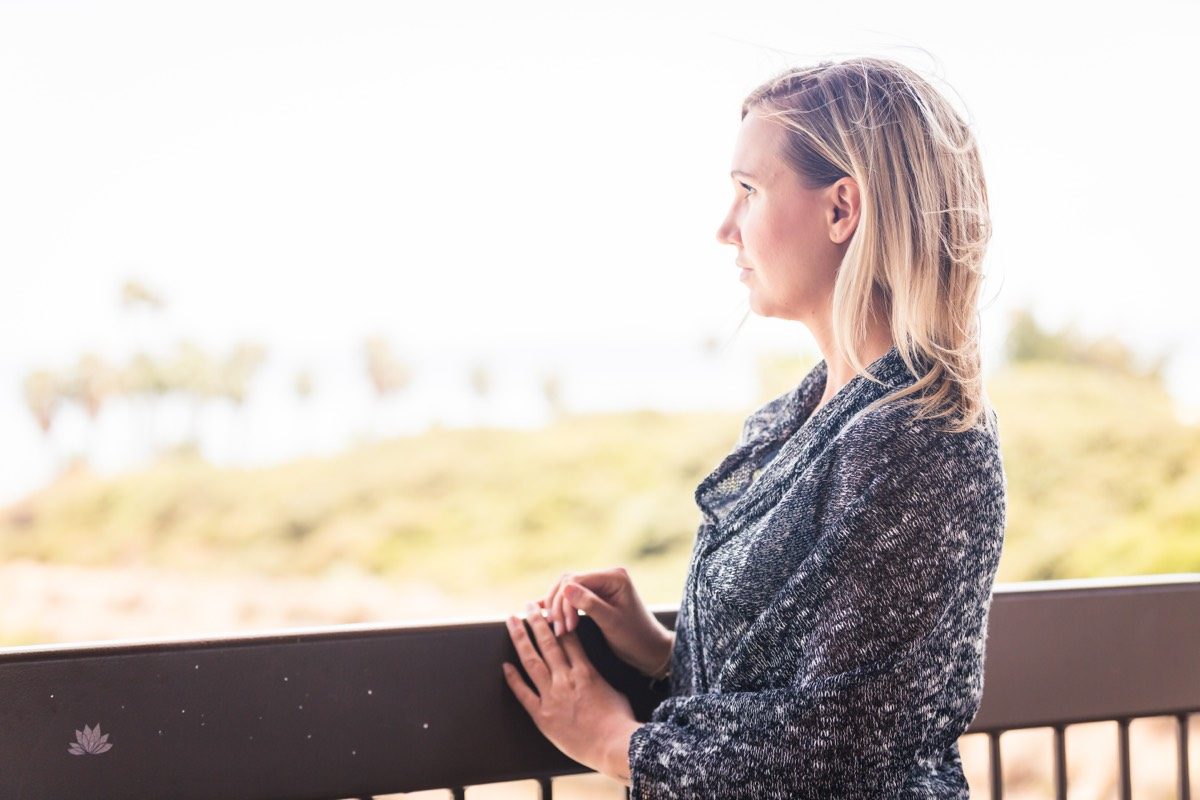 Woman with blonde hair at a balcony rail gazing out over the hazy coast
